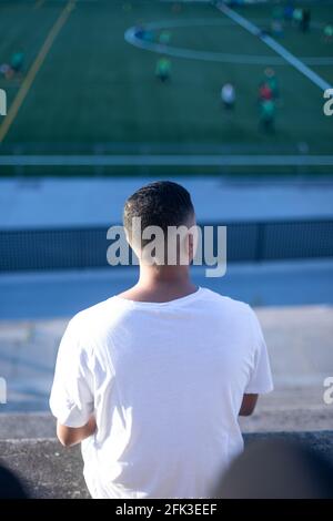 Un giovane bell'uomo in t-shirt e jeans si siede sopra uno stadio sbiancante da solo Foto Stock