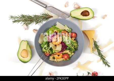 Vista dall'alto dell'appetitosa insalata con pasta e con gustosi gamberi e avocado in un bel piatto blu su sfondo bianco. Concetto di nutrizione adeguata per mantenere il peso corporeo. Foto Stock