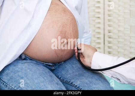 il medico esamina una donna incinta ascoltando il feto battito cardiaco con fonendoscopio Foto Stock