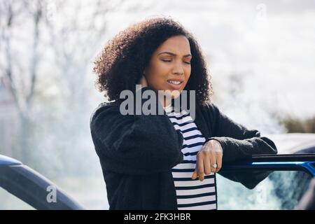 Giovane donna strofinando il collo nel dolore da ferita del whiplash in piedi da auto danneggiata dopo un incidente stradale Foto Stock