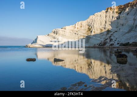 Realmonte, Agrigento, Sicilia, Italia. Vista attraverso la baia fino alla Scala dei Turchi, la mattina presto, bianche scogliere calcaree riflesse in un mare tranquillo. Foto Stock