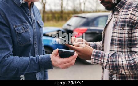 I conducenti più giovani e più anziani al lato del cambio di strada assicurazione auto dettagli dopo l'incidente stradale utilizzando telefoni cellulari Foto Stock