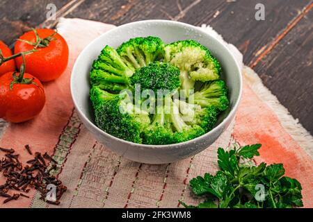 Mazzi di broccoli verdi pronti a cucinare. Broccoli in una piastra bianca su un tavolo di legno Foto Stock