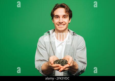 Il giovane uomo tiene in mano i semi di girasole, isolati su sfondo verde Foto Stock