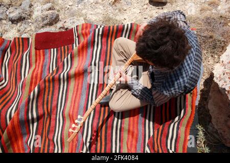 Uomo che suona il tradizionale strumento musicale turco (Saz). Tappeti tessuti. Foto Stock