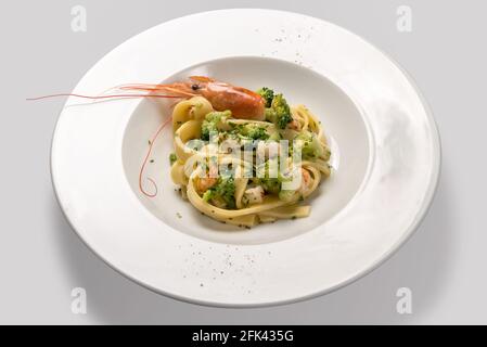 Tagliatelle di pasta con gamberi, gamberi e broccoli in piastra bianca isolata su fondo grigio chiaro Foto Stock