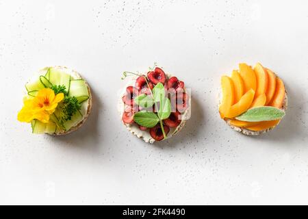 Riso croccato con diversi condimenti bacche e verdure su sfondo bianco. Snack estivo sano. Disposizione piatta. Foto Stock