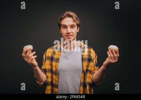 Il giovane biondo in camicia gialla tiene i funghi in entrambe le mani, isolato su sfondo nero Foto Stock