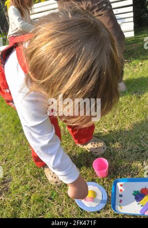 bambino visto dall'alto, giocando con piccoli piatti e occhiali di plastica, con giardiniere rosso e pantofole di gomma Foto Stock