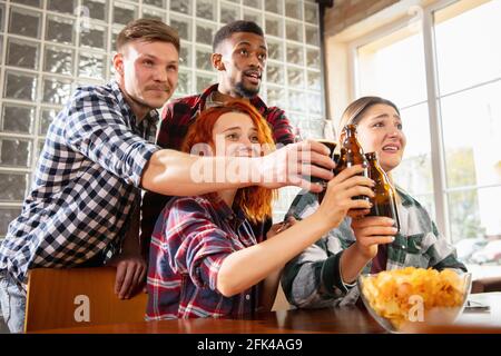 Gruppo di amici che guardano la partita sportiva insieme. Tifosi emotivi che si acclamano per la squadra preferita, guardando una partita emozionante. Concetto di amicizia, tempo libero Foto Stock