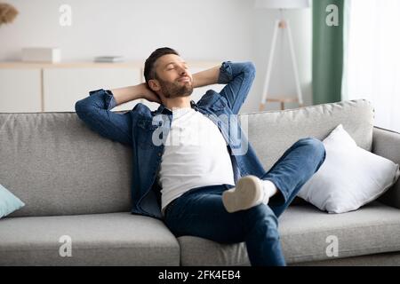 Felice uomo bearded che si rilassa sul divano a casa Foto Stock