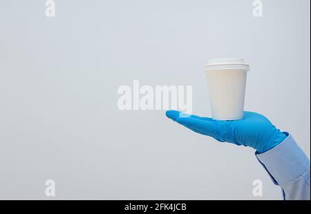 Indossare guanti medici che trasportano caffè in tazza di carta. Banner, spazio per la copia. Servizio di consegna senza contatto durante la quarantena coronavirus pandemia. Prendi Foto Stock