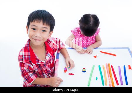 Piccoli bambini asiatici che giocano e creano giocattoli dall'impasto da gioco sul tavolo. Ragazzo sorridendo e guardando la macchina fotografica, su sfondo bianco. Rafforzare le immagini Foto Stock