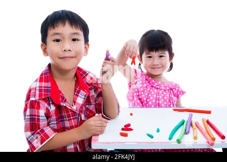 Piccoli bambini asiatici che giocano e creano giocattoli dall'impasto da gioco sul tavolo. Ragazzo e ragazza sorridenti e mostrano opere di argilla a macchina fotografica, su sfondo bianco Foto Stock