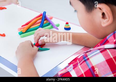 Piccolo ragazzo asiatico che gioca e crea giocattoli dall'impasto da gioco. Robot di modellazione dell'argilla per lo stampaggio di bambini. Rafforzare l'immaginazione del bambino Foto Stock