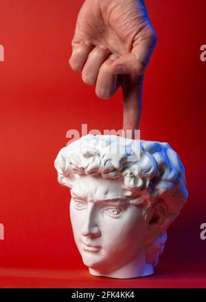Vaso in gesso sotto forma di testa di Davide e mano maschio su sfondo rosso. Foto Stock