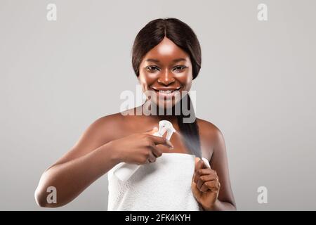 Cura quotidiana dei capelli. Ritratto di sorridente afroamericana femmina applicando Hairspray idratante Foto Stock