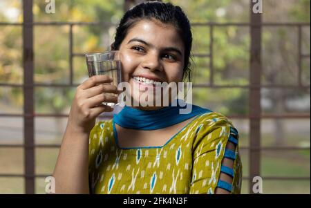 Una donna indiana asiatica sorridente con un bicchiere di freddo acqua che tocca la guancia Foto Stock