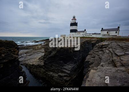 Antico faro Hook paesaggio con scogliere e le onde e penisola Centro storico a Wexford, Irlanda. Foto Stock