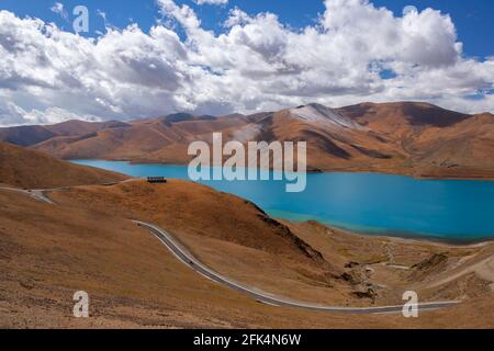 Le acque glaciali blu brillante del lago Yamdrok e la strada del passo alto (16860 piedi) in Tibet. Foto Stock