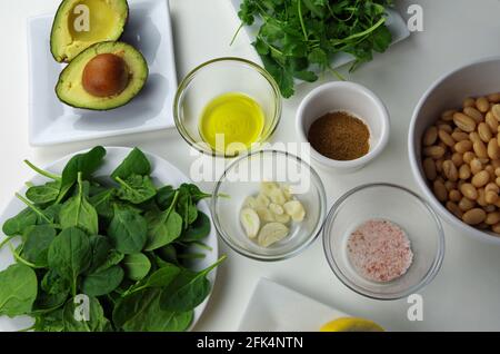 Ingredienti alimentari sani utilizzati per preparare un tuffo delizioso, tra cui avocado, olio d'oliva, aglio, cumino, sale rosa, fagioli, spinaci, coriandolo e limone Foto Stock