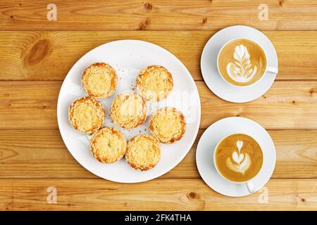 Cupcake fatti in casa appena sfornati e due tazze di cappuccino di caffè su un tavolo di legno. Vista dall'alto. Foto Stock