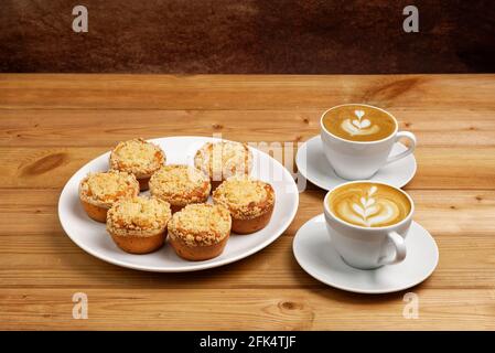 Cupcake fatti in casa appena sfornati e due tazze di cappuccino di caffè su un tavolo di legno. Foto Stock
