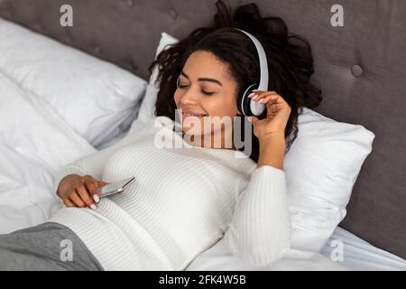 Soddisfatta giovane donna nera che ascolta la musica Foto Stock