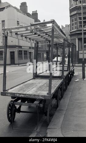 Anni ottanta, molti dei commercianti di legno incorniciati di metallo vuoti di mercato stalli o carrelli di esposizione sulle ruote, parcheggiati su una strada accanto ad un marciapiede, in Whitecross Street, Islington, Londra, EC1Y, Inghilterra, Regno Unito. E' caratterizzato da un famoso mercato di strada, uno dei mercati piu' vecchi di Londra, che ha esistito da oltre 150 anni. Foto Stock