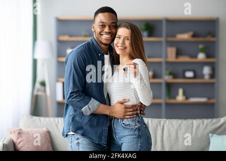 Felice giovane coppia multirazziale tenendo le chiavi di casa e abbracciando Foto Stock