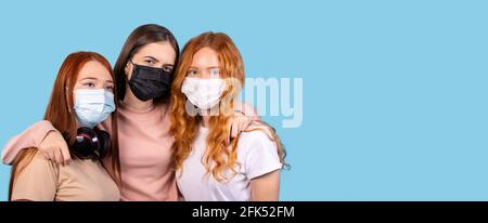 Ritratto di tre amici che indossano maschere protettive su sfondo blu. Foto Stock