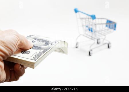 La mano umana tiene un pacchetto di 100 dollari fatture e carrello di shopping su sfondo sfocato. Concetto di shopping, vendita, Black Friday, Cyber Monday. Foto Stock