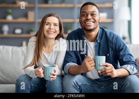 Weekend di svago. Giovane coppia allegra multiculturale che si rilassa in soggiorno Foto Stock