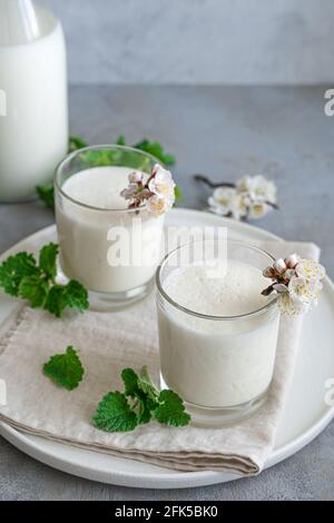 Yogurt fresco fatto in casa in due bicchieri con erbe e fiori su sfondo grigio. Foto Stock
