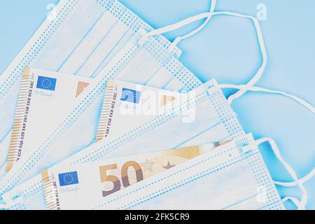 Maschere mediche monouso e banconote in euro su sfondo azzurro. Vista dall'alto Foto Stock