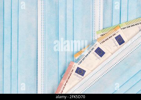 Maschere mediche monouso e banconote in euro su sfondo azzurro. Vista dall'alto Foto Stock