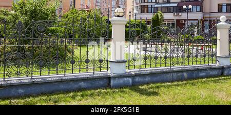 Recinzione in ferro battuto. Immagine di una bella recinzione decorativa in ghisa con forgiatura artistica e colonne in pietra Foto Stock