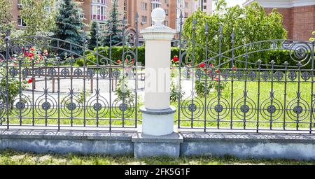 Recinzione in ferro battuto. Immagine di una bella recinzione decorativa in ghisa con forgiatura artistica e colonne in pietra Foto Stock