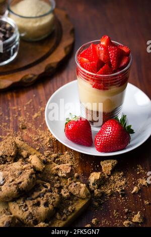 Dessert trifle di fragole con budino e biscotti su legno scuro sfondo con vasi di vetro Foto Stock