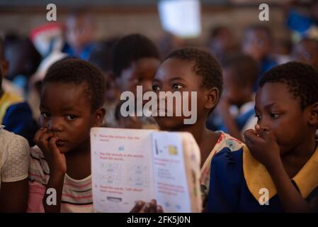 Mzuzu, Malawi. 30-05-2018. Ritratto di una ragazza nera che mostra il suo libro di testo alla sua insegnante in classe affollata di bambini in una scuola rurale in Malawi. Foto Stock