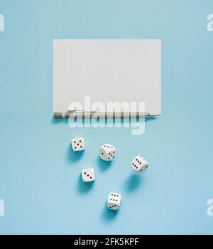 Gioco di Yahtzee in corso. Dadi rotolante, matita e foglio di punteggio su sfondo blu. Concetto astratto con spazio di copia. Disposizione piatta. Foto Stock