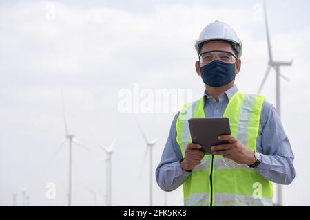 Ingegnere mulini a vento indossare maschera viso e compressa di calettamento con vento turbina in background Foto Stock