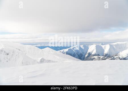 Panoramica panoramica delle montagne innevate a Zakopane, Polonia. Paesaggio invernale innevato. Lo scatto viene effettuato durante il giorno. Cielo pieno di nuvole bianche sullo sfondo. Neve-coperto paesaggio sloppy. Foto Stock