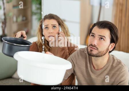 la coppia impressionabile raccoglie l'acqua che perde dal soffitto mentre telefona l'idraulico Foto Stock