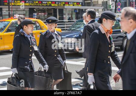 Tre assistenti di volo fuori servizio femminili che indossano uniformi che attraversano l'attraversamento trafficato della zebra a Ginza, Tokyo, Giappone Foto Stock