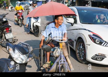 Vietnamita uomo con gamba di legno che si ruota lungo la strada in una sedia a rotelle, Hoi An, Vietnam Foto Stock