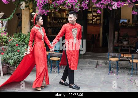 Coppia vietnamita in rosso Ao dai che cammina nella città vecchia, Hoi An, Vietnam Foto Stock