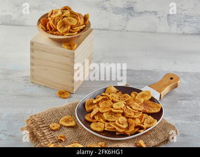 Bananine chips cibo sano, frutta secca e patatine vegetali sane, spuntini vegani sani su burlap in un piatto e stand di legno Foto Stock