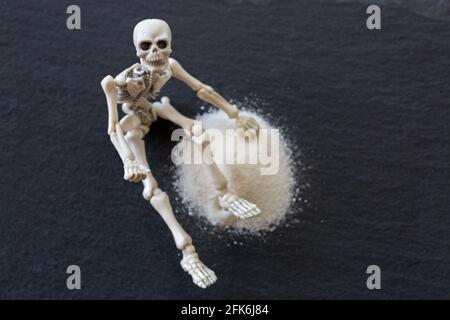 Soft focus scheletro bianco ossa del corpo morto seduta accanto a. polvere bianca fine pericolosa come cocaina su fondo di pietra nera Foto Stock