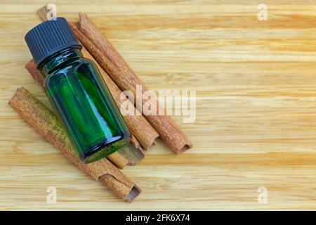 Estratto di olio concentrato puro alla cannella in bottiglia verde Bastoni di cannella su sfondo di legno con copyspace Foto Stock